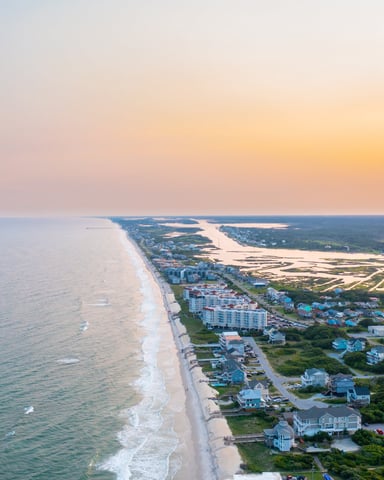 Aerial view of coastal town at sunset with sandy beach, ocean, residential homes, and marshland extending inland