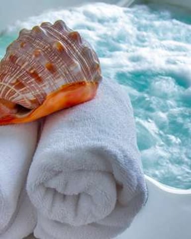 Large seashell and rolled white towels arranged on hot tub edge with turquoise water and jets visible