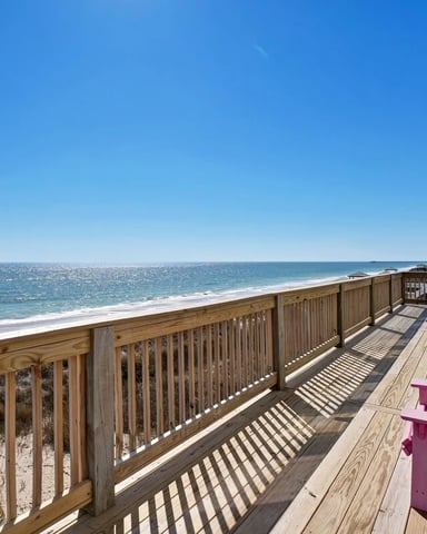 Beachfront deck with wooden railing, pink and green Adirondack chairs, ocean and sandy beach view