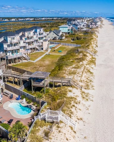 Aerial view of beachfront homes with pool, sandy beach, ocean, and coastal town in distance