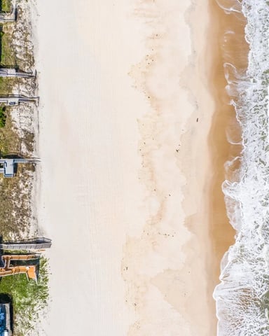 Aerial view of beachfront houses with blue roofs along sandy beach and ocean waves