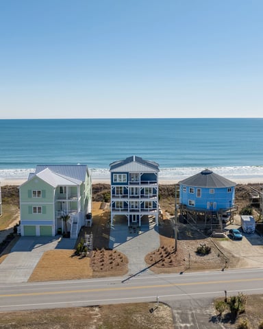 Colorful beachfront vacation homes on stilts facing ocean with sandy beach and clear sky