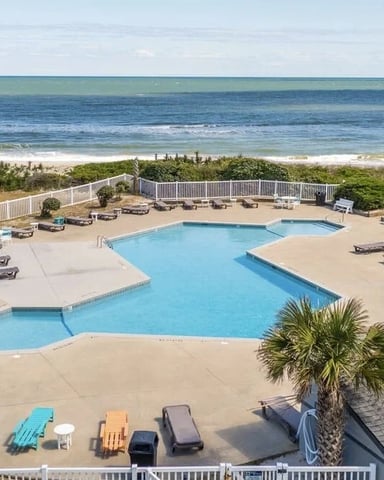 Oceanfront pool complex with loungers, beach access, and white beach house with dune vegetation