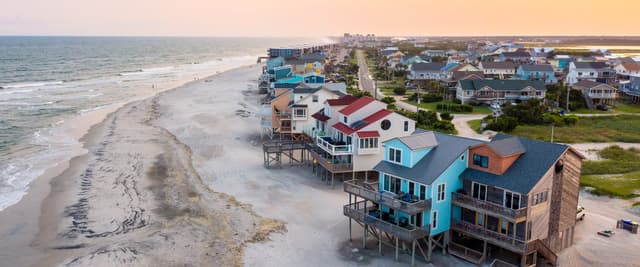 Aerial view of colorful beachfront houses on stilts along sandy shore at sunset