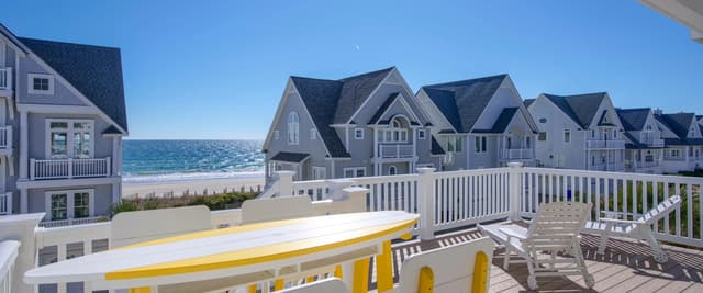 Beachfront deck with yellow and white furniture overlooking row of gray beach houses and ocean