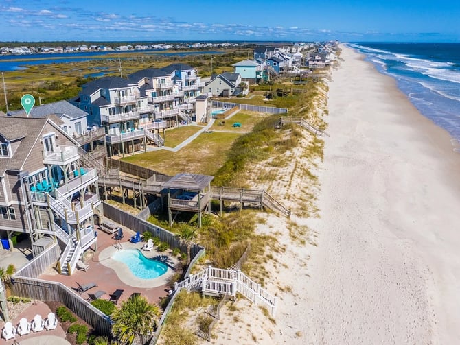 Aerial view of beachfront vacation homes with pool, sandy beach, and ocean waves along the coast.
