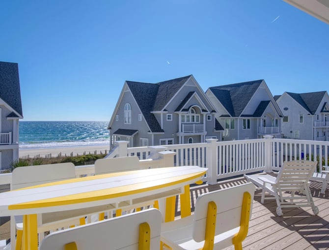 Beachfront deck with yellow and white railings, lounge chairs, and row of gray beach houses with ocean view